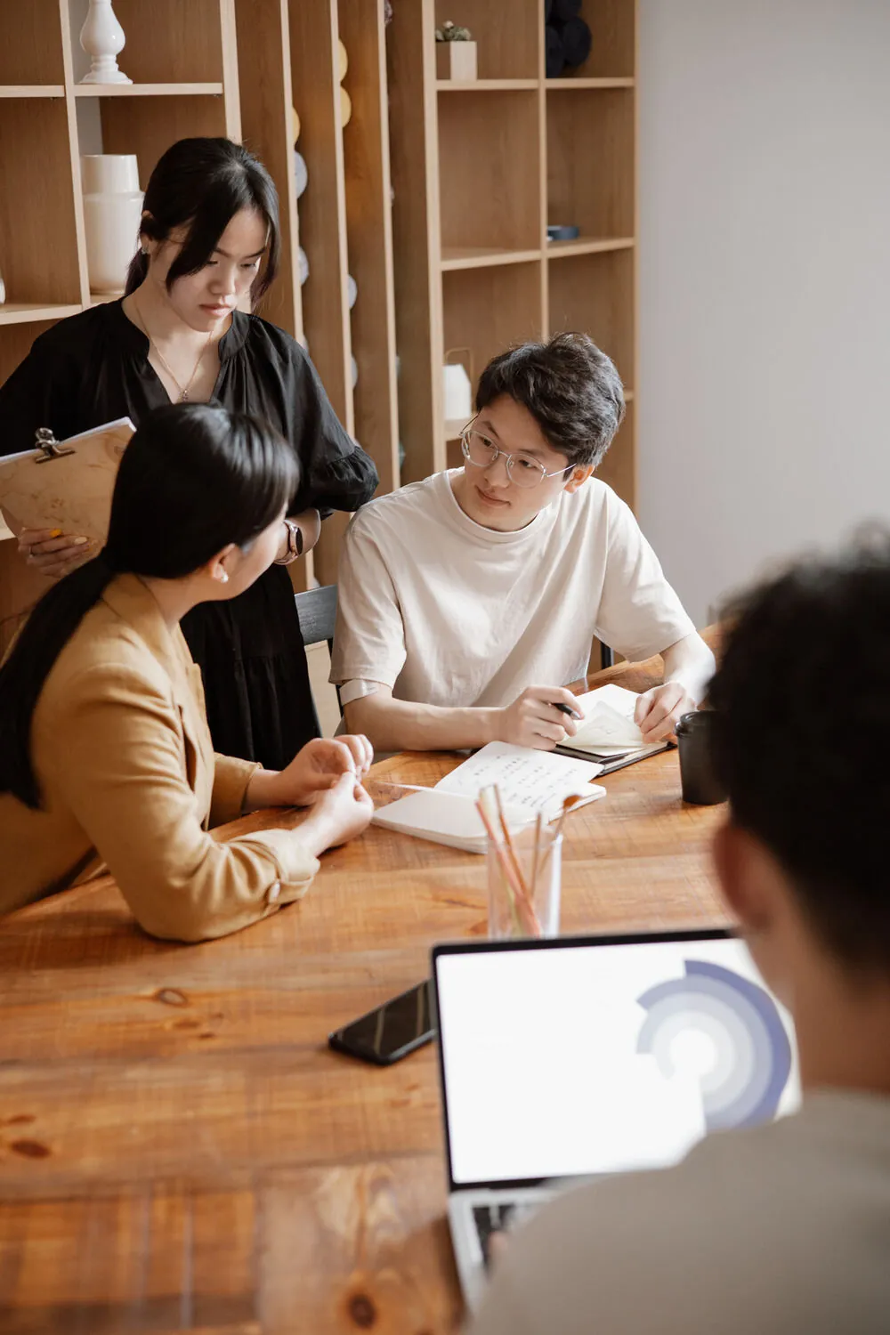 A small creative team gathered around a wooden table reviewing notes and a laptop.